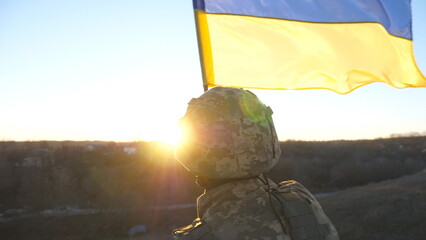Dolly shot of male ukrainian army soldier lifting national banner in hill. Young man in military...