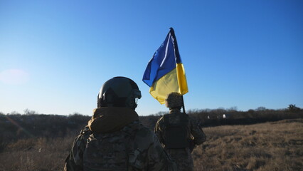 Female and male soldier of ukrainian army walking with flag of Ukraine at field. Woman and man in military uniform going with national banner at meadow as sign of victory against russian aggression