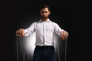 Man in formal outfit pulling strings of puppet on dark background, low angle view