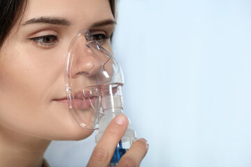 Sick young woman using nebulizer on blurred background, closeup. Space for text