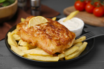 Tasty soda water battered fish, lemon slice and potato chips on dark wooden table