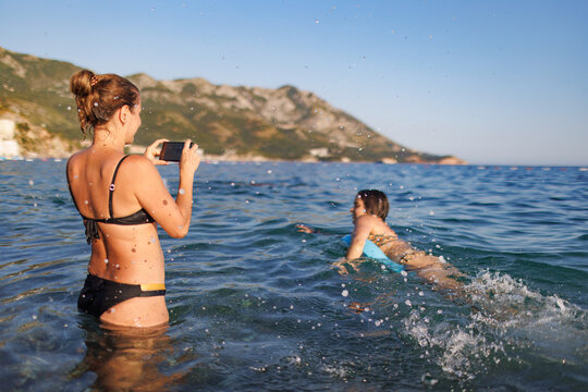 A young mother photographs her daughter on an inflatable ring in the sea