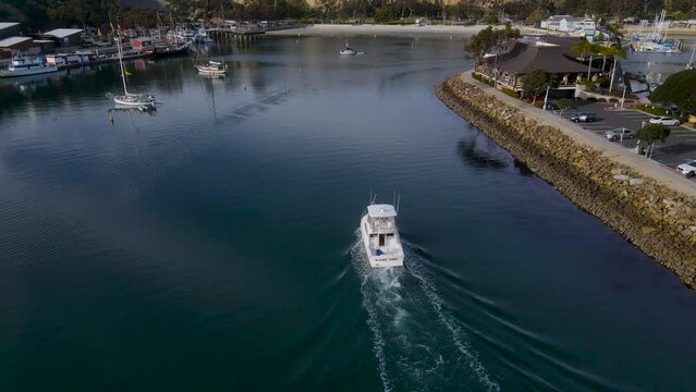 Rear aerial view of boat entering harbor with small ripples from wake