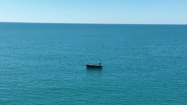 Lone person pulls in line while standing on boat in the open ocean