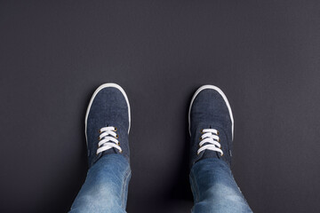 Child in stylish sneakers standing on black background, top view