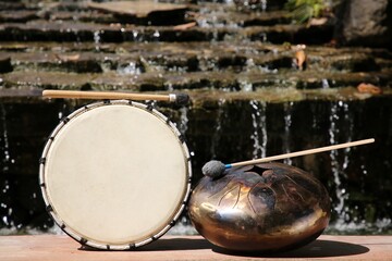 Drum and handpan with mallets near waterfall outdoors on sunny day. Percussion musical instruments