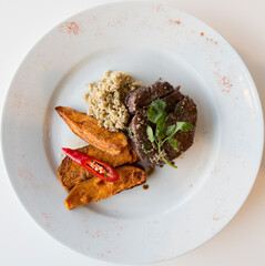 Grilled steak with sweet potato, cuscus & red chilli on a white plate.