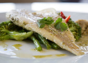 Healthy closeup photo of sea bass with green vegetables topped with coriander.