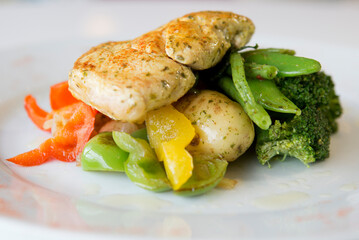 Close up photo of grilled chicken with pepper salad, potato & green vegetables.