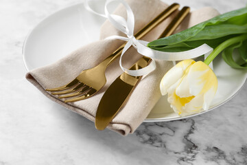 Fototapeta na wymiar Stylish table setting with cutlery and tulip on white marble background, closeup