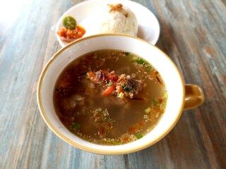 Sop iga or beef short ribs soup in a white bowl with a plate of rice which are carrot and cabbage. Meat and vegetable soup in a white bowl, as protein, vitamin, and fiber source