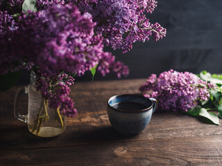 Spring composition, blooming lilac bouquet and a cup of coffee on a wooden table