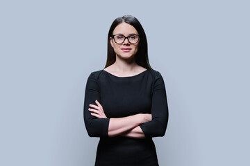 Young woman in glasses in black dress posing on gray background