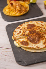 Quesadilla sobre pizarra negra y mesa de madera, con queso derretido y tortilla de trigo dorada.