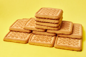 A pile of square cookies on a yellow background. A tasty and sweet snack.