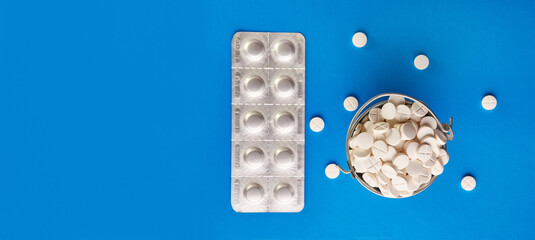 A small metal bucket filled with pills on a blue background. Concept of drug abuse and overdose.