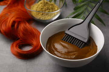 Bowl of henna cream, brush and red strand on light grey table, closeup. Natural hair coloring