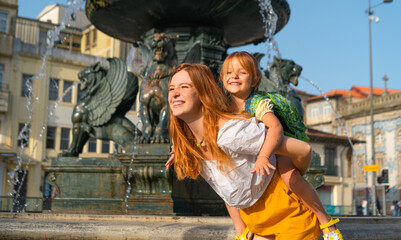 Fototapeta na wymiar Lovely red haired mother and little daughter playing near the fountain in the old European town.