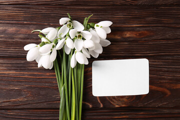 Beautiful snowdrops and paper card on wooden table, flat lay. Space for text