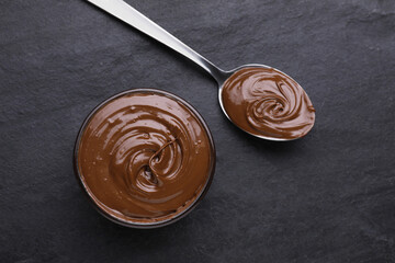 Bowl and spoon with tasty chocolate paste on black textured table, flat lay