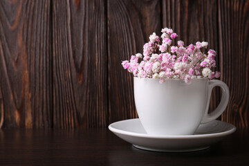 Obraz na płótnie Canvas Beautiful dyed gypsophila flowers in white cup on wooden table. Space for text
