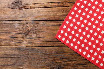 Red checkered tablecloth on wooden table, top view. Space for text