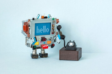 A toy robot retro computer holds a handset of an old vintage rotary phone. The concept of analog...