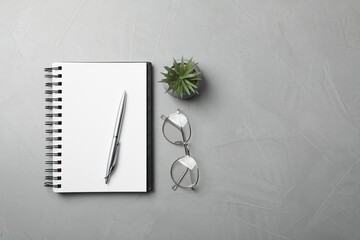 Ballpoint pen, notebook and glasses on light gray table, flat lay. Space for text