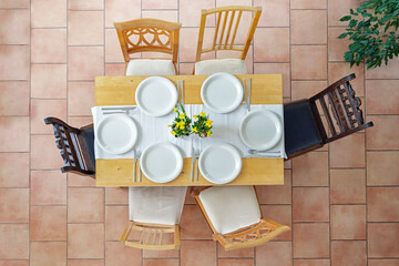 Top view of a place setting with six white plates, cutlery and yellow daffodil flowers on a light...