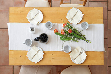 Setting for an afternoon coffee break with four plates, cups, napkins, coffee pot and tulip flowers...