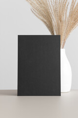 Black invitation card mockup with a reed  pampas decoration on the beige table. 5x7 ratio, similar...