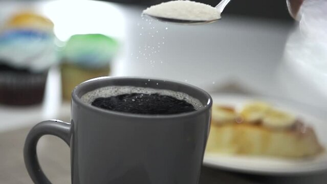 Sugar crystals falling from tablespoon to cup of coffee - slow motion