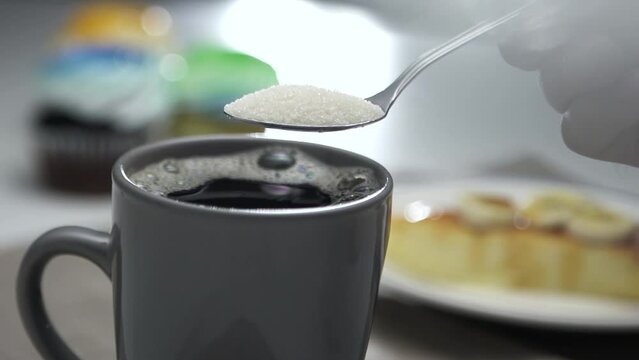 Sugar crystals falling from tablespoon to cup of coffee - slow motion