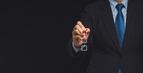 Businessman holding a pen and checking a mark on the boxes symbol is one of three options while standing on a black background