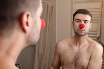 Man wearing clown nose looking at his reflection 