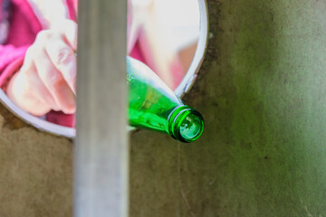 Throwing empty green glass bottle into recycle bin garbage container. Nature love, waste sorting and recycling concept idea. Lady caring about environment.