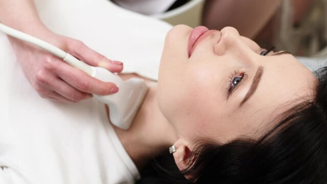 Ultrasound diagnosis of the thyroid gland of a young woman in the clinic. A female doctor holds an ultrasound probe along the patient's neck. Health concept.