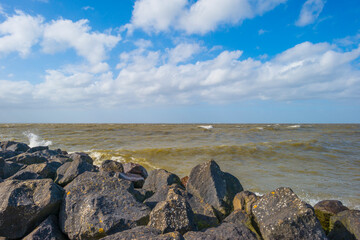 Fototapeta na wymiar Dike along a stormy lake below a blue sky and white clouds in winter, Markerwaard, Almere, Flevoland, The Netherlands, March 13, 2023