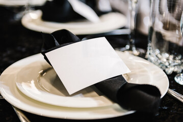 Serving, setting table. Plate decorated linen black napkin, postcard, silverware cutlery, glasses. Side view. Closeup. Wedding set up, dinner table reception. Birthday, baptism, event.