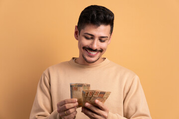 cheerful brazilian man with brazil banknotes currency in beige background. business, loan, pay, wealth concept.  - obrazy, fototapety, plakaty