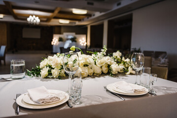 Festive table covered tablecloth, decorated composition flowers and candles in party area. Wedding setup detail. Table setting, serving. Banquet decoration in hall restaurant. Luxury reception.