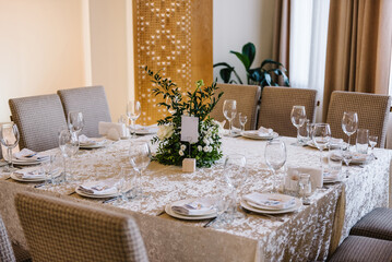 Wedding set up, dinner table reception. A plate with a napkin, knives and forks next to the plate. Flower composition with greenery leaves in center of table. Banquet decoration in hall restaurant.