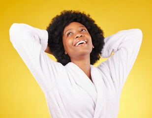 Black woman relax, bathrobe and happiness in a studio ready for luxury spa treatment for self care. Isolated, yellow background and happy young female with a smile from skincare and wellness