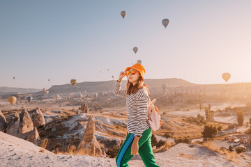 Happy traveller girl walking against background of magnificent flying hot air balloons in famous...