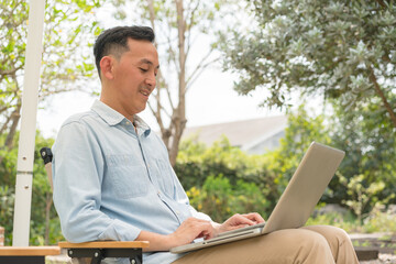 A man working with laptop remotely from home. A distant work place with many home plants. Person working from garden.