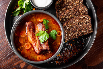 Solyanka soup with meat, sausage, vegetables, olives and lemon in bowl on wooden table background
