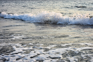 Sea waves crashing against the shore. Wild white sea foams on the sand 
