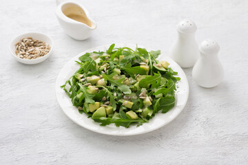 Fresh salad of arugula, cucumbers and avocados with yogurt dressing and seeds on a light gray background. Delicious homemade food