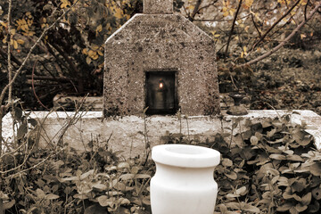 A nameless orthodox tombstone alone among the trees in autumn. An oil lamp is burning inside the tombstone