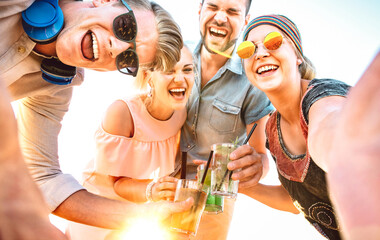 Trendy people group taking selfie at spring break festival toasting fancy cocktails at sunset - Summer joy and friendship concept with young friends on happy hour time - Bright sunshine filter
